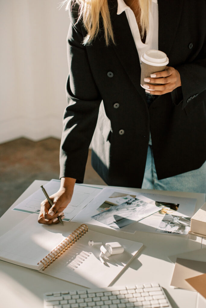 African American woman writing out her creative direction while holding a cup of coffee. 